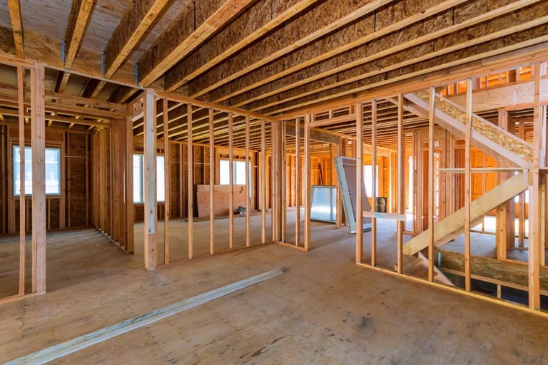 Interior of residential home under construction showing wooden framing, beams, studs, and unfinished drywall