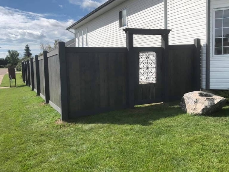 Black wooden fence with gate enclosing yard area next to white house with green lawn